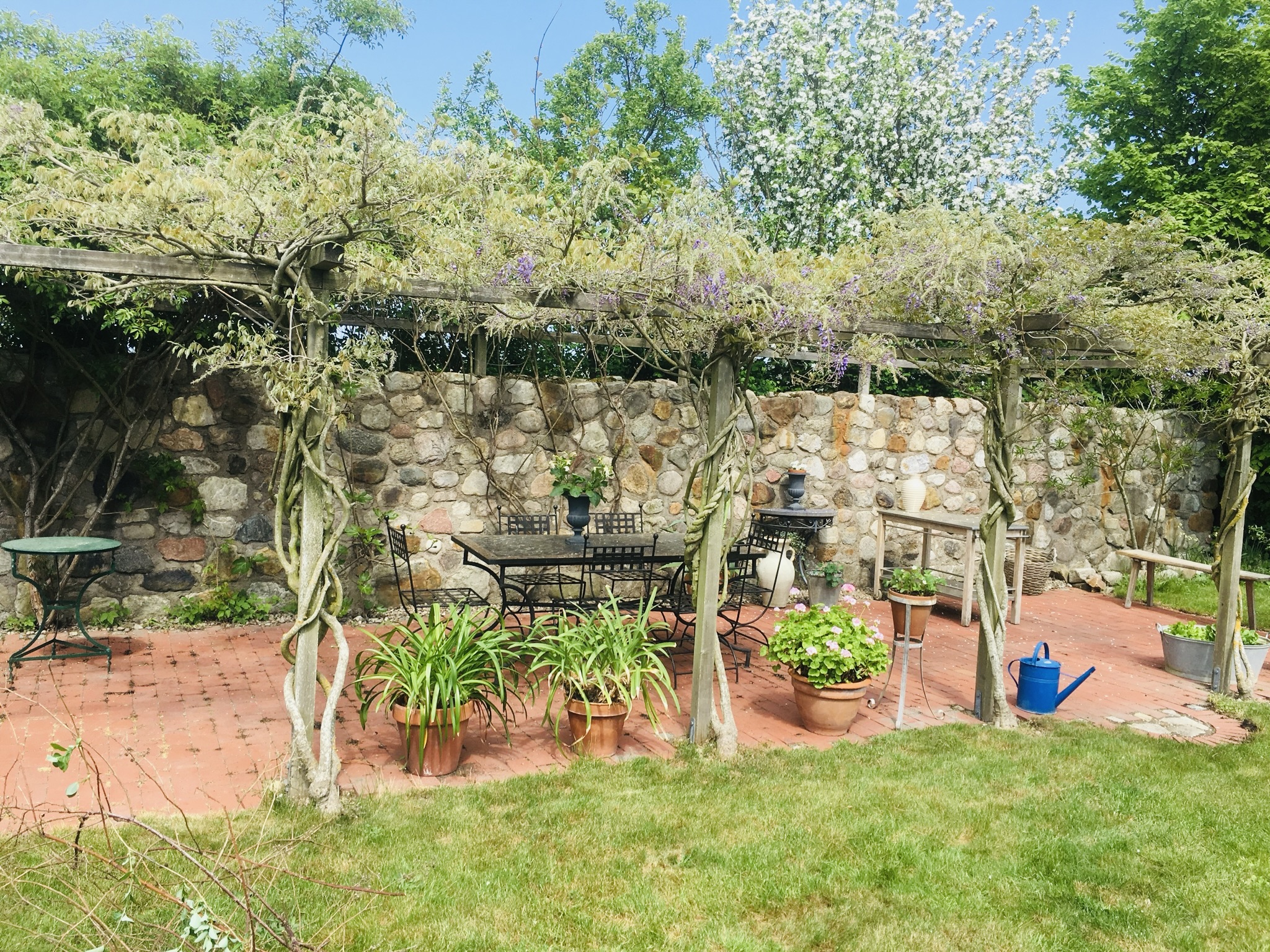 Uteplats under pergola med naturstensmur och blommande klängväxter