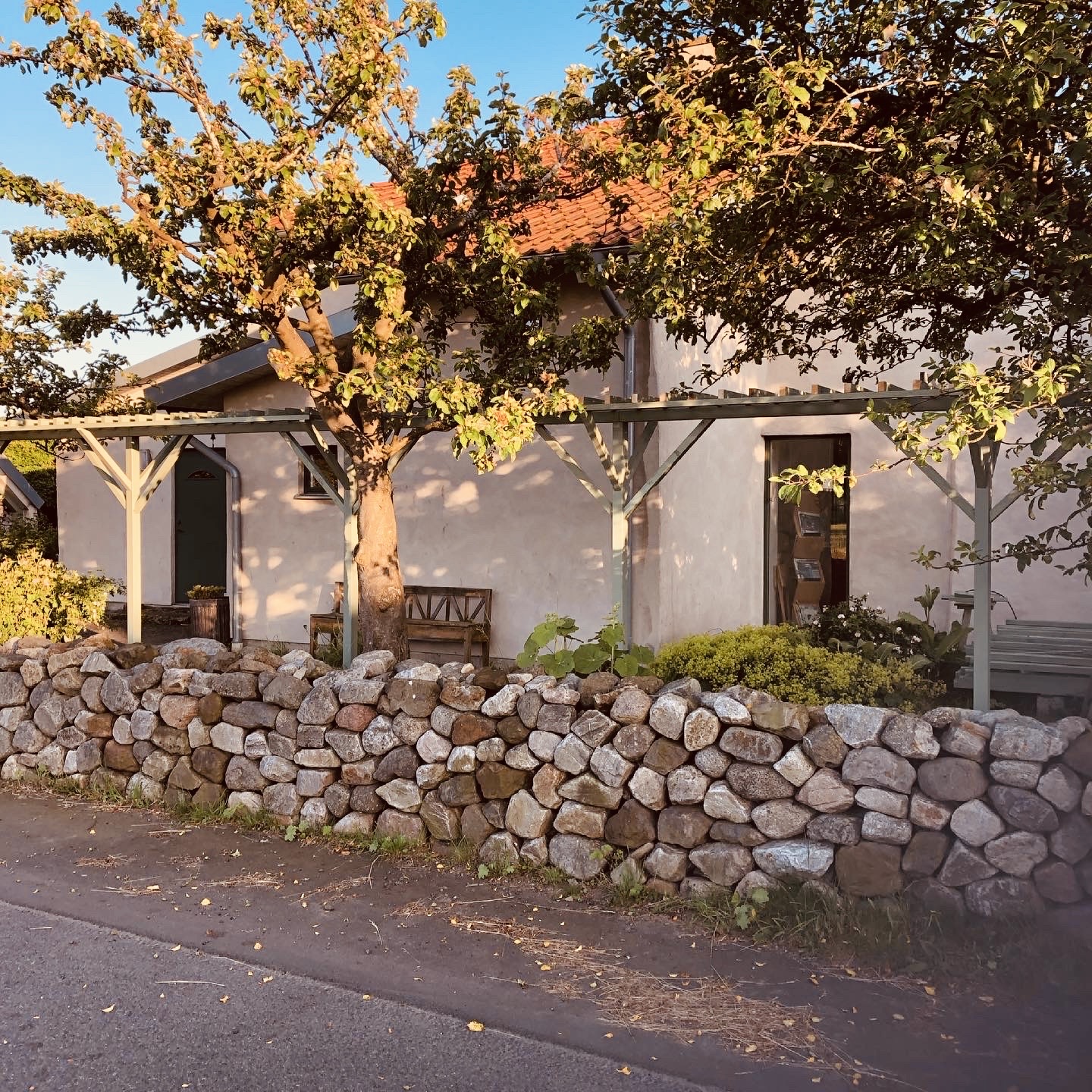 Torrmurad naturstensmur framför vitputsat hus med pergola, Brantevik